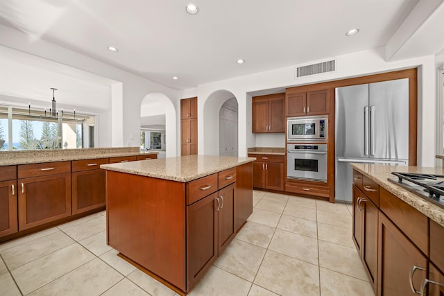 kitchen featuring visible vents, decorative light fixtures, a center island, light stone countertops, and stainless steel appliances