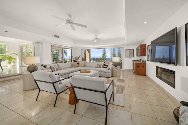 living area with light tile patterned floors, recessed lighting, visible vents, a tray ceiling, and a glass covered fireplace