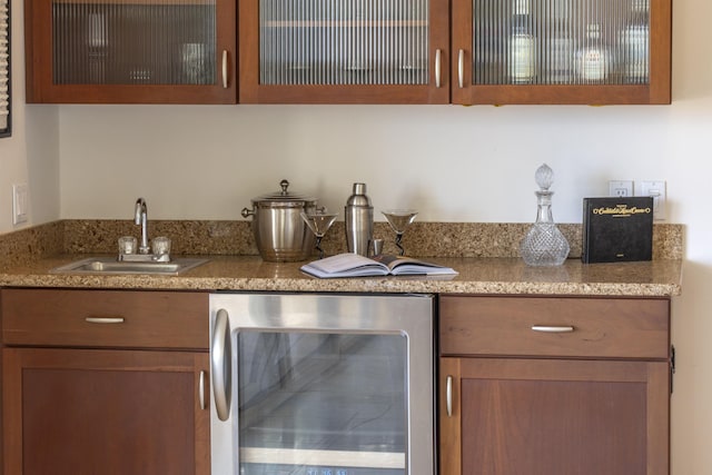 kitchen featuring beverage cooler, brown cabinetry, a sink, and glass insert cabinets