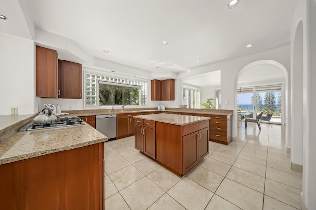 kitchen with appliances with stainless steel finishes, brown cabinets, light stone counters, and a center island