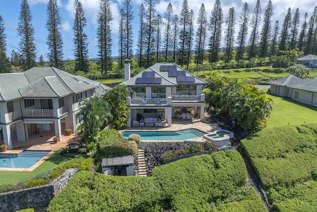 rear view of house with a balcony, a patio area, a pool with connected hot tub, and solar panels