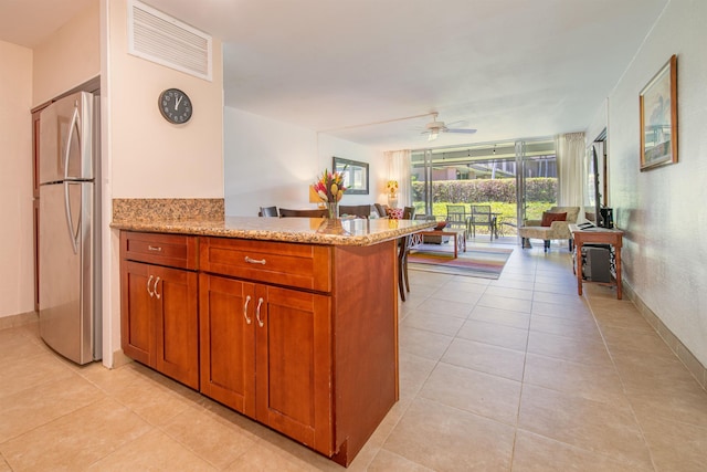 kitchen featuring light tile patterned flooring, stainless steel refrigerator, ceiling fan, kitchen peninsula, and light stone countertops