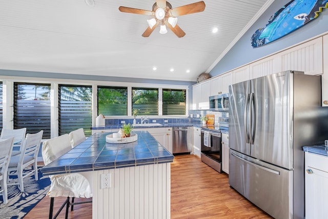 kitchen with a kitchen breakfast bar, white cabinets, appliances with stainless steel finishes, tile counters, and a center island