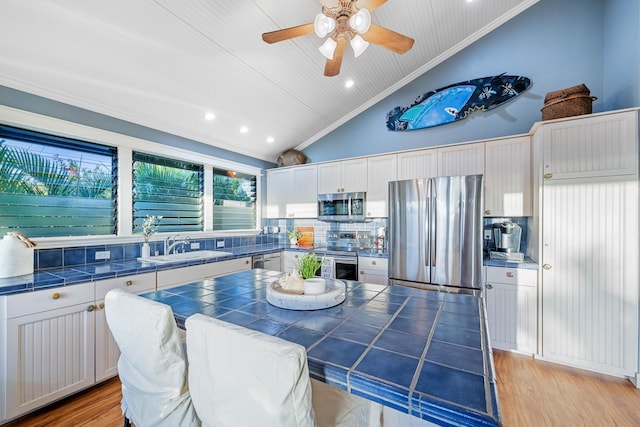 kitchen with appliances with stainless steel finishes, light wood-type flooring, white cabinetry, and tile countertops