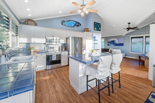 kitchen with a breakfast bar, tile countertops, stainless steel appliances, white cabinetry, and a sink