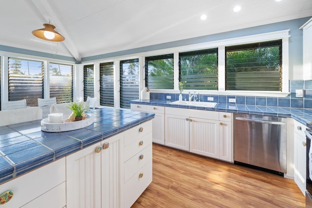 kitchen with white cabinets, dishwasher, tile countertops, vaulted ceiling, and a sink