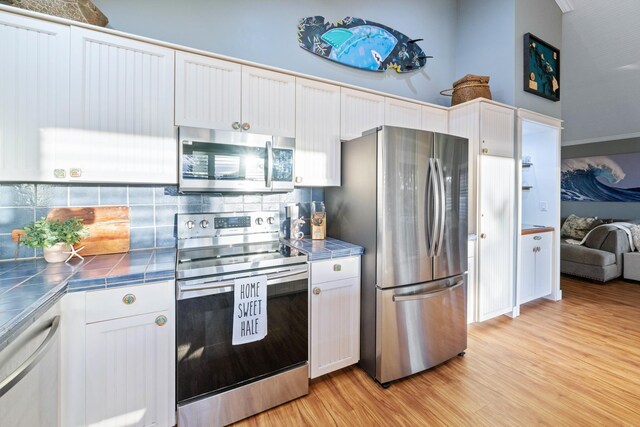 kitchen with light wood finished floors, stainless steel appliances, tile counters, tasteful backsplash, and white cabinets