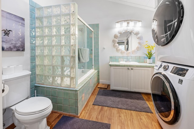 full bathroom with stacked washer / dryer, toilet, wood finished floors, tiled shower / bath, and vanity