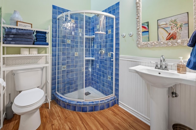 bathroom featuring toilet, wainscoting, a sink, a shower stall, and wood finished floors