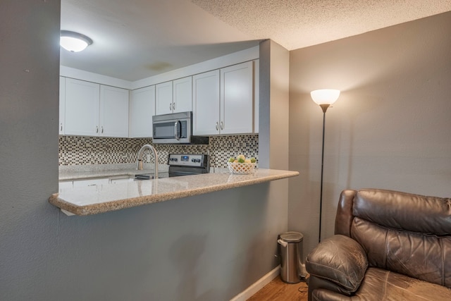 kitchen with stainless steel appliances, white cabinets, light hardwood / wood-style floors, kitchen peninsula, and backsplash