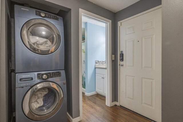laundry area with stacked washer / drying machine, dark wood-style flooring, laundry area, and baseboards
