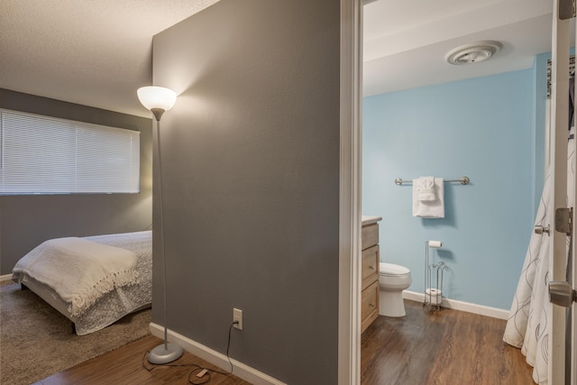 bedroom featuring baseboards, visible vents, ensuite bathroom, and dark wood-type flooring