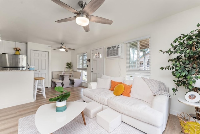 living area with an AC wall unit, a ceiling fan, and light wood-style floors