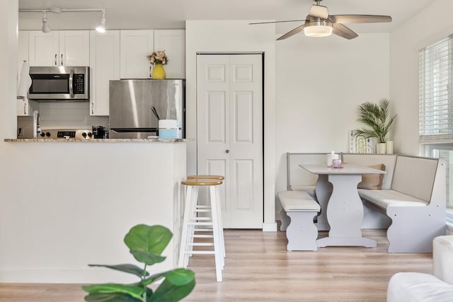 kitchen with white cabinets, appliances with stainless steel finishes, light wood-style floors, a ceiling fan, and tasteful backsplash