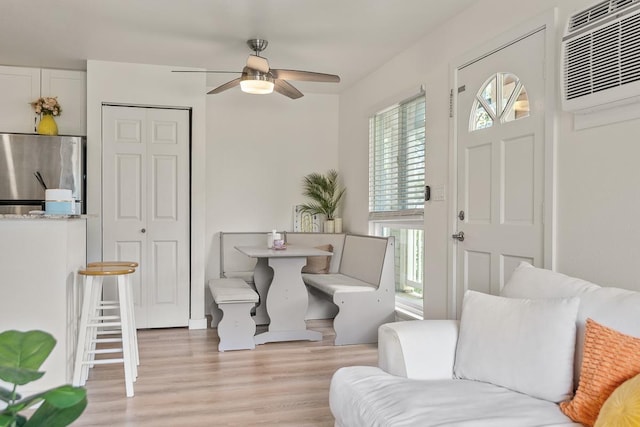 living room featuring light wood-style floors, ceiling fan, and a wall unit AC