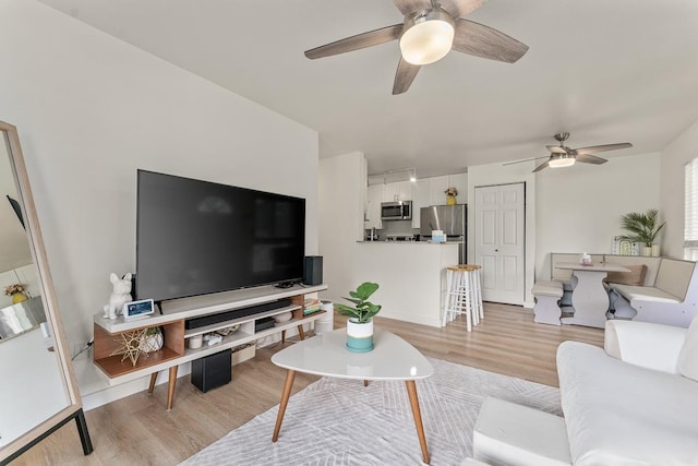 living room with baseboards, a ceiling fan, and light wood-type flooring