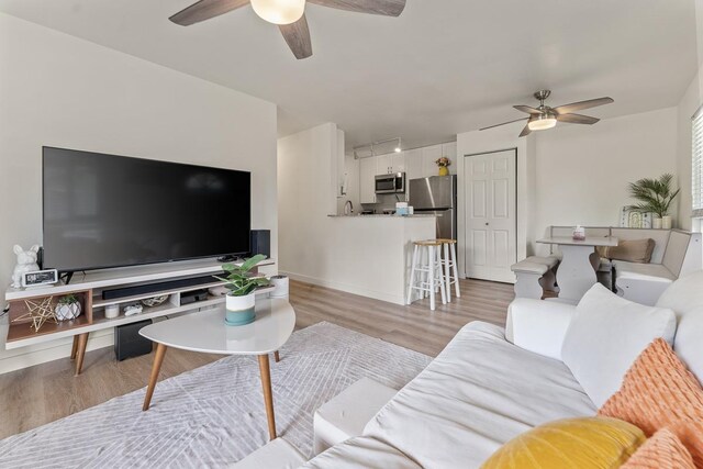 living area with a ceiling fan, baseboards, and light wood-style floors