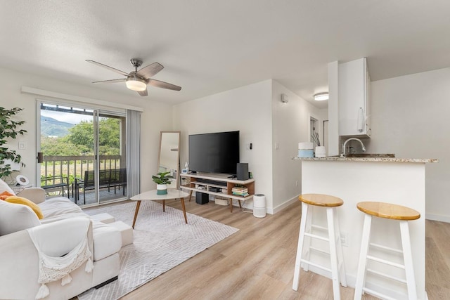 living area featuring baseboards, a ceiling fan, and light wood finished floors