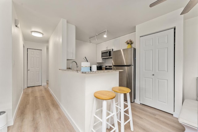 kitchen featuring white cabinets, a kitchen breakfast bar, appliances with stainless steel finishes, and light wood-style floors