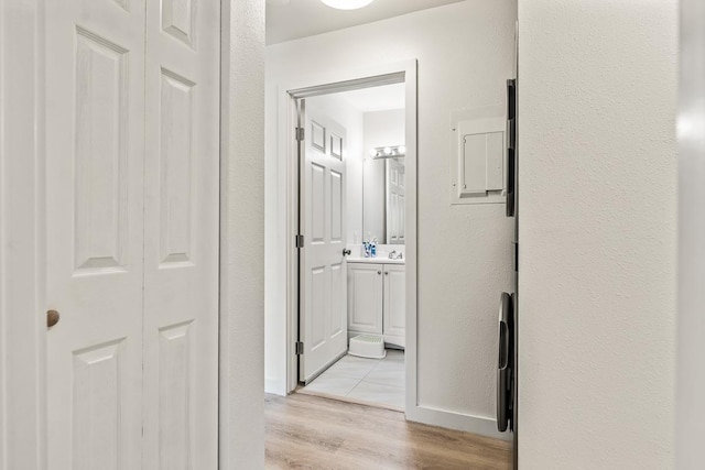 corridor with light wood-style floors, baseboards, and a textured wall
