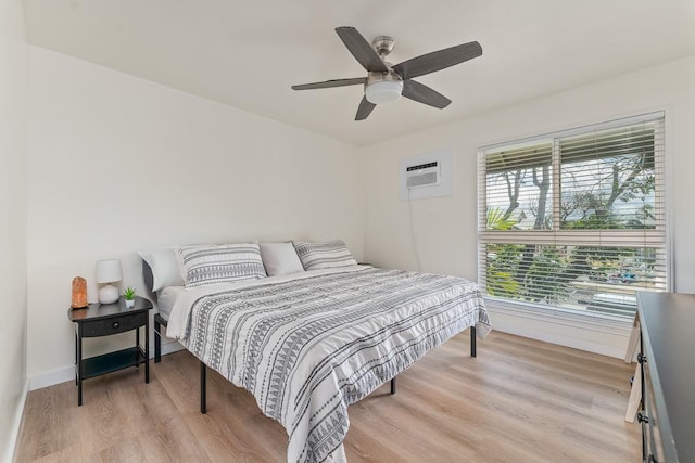 bedroom featuring baseboards, a ceiling fan, light wood-style flooring, and a wall unit AC