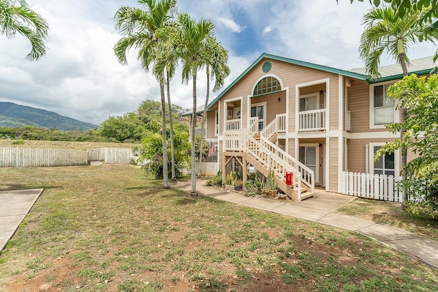 view of front of home with covered porch, a front yard, fence, a mountain view, and stairs