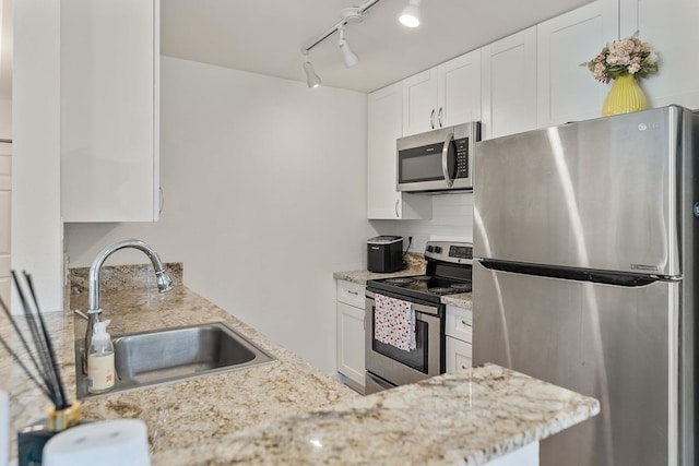 kitchen featuring appliances with stainless steel finishes, a sink, light stone counters, track lighting, and white cabinetry