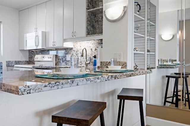 kitchen featuring decorative backsplash, a kitchen breakfast bar, kitchen peninsula, white cabinets, and white appliances