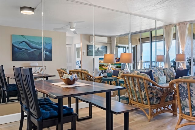 dining area with ceiling fan, a wall mounted AC, a textured ceiling, and light wood-type flooring