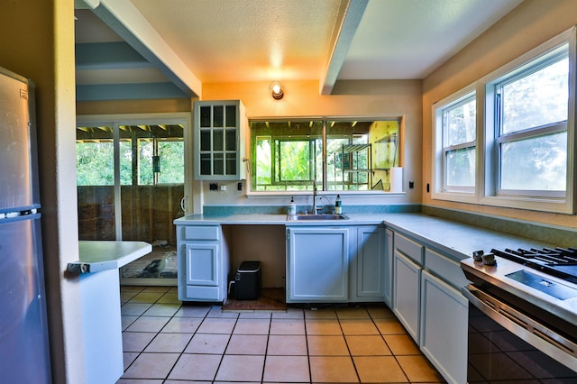 kitchen with appliances with stainless steel finishes, sink, light tile patterned flooring, a textured ceiling, and white cabinetry