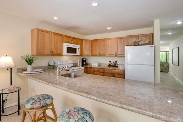 kitchen with sink, kitchen peninsula, light stone countertops, a kitchen bar, and white appliances