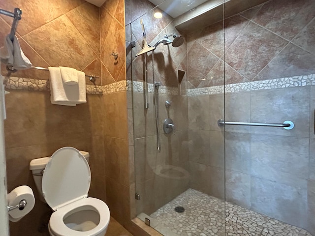 bathroom with tile walls, toilet, and a shower with shower door