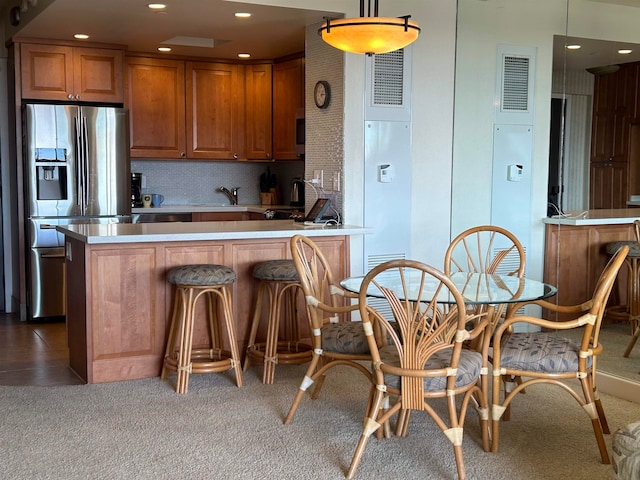 kitchen featuring sink, hanging light fixtures, dark wood-type flooring, a kitchen bar, and stainless steel refrigerator with ice dispenser