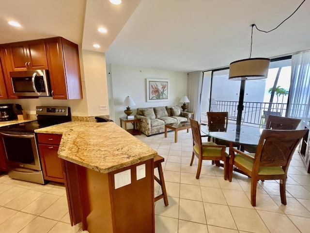 kitchen with hanging light fixtures, light stone counters, kitchen peninsula, light tile patterned floors, and appliances with stainless steel finishes