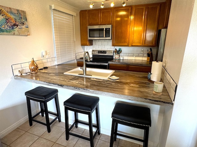 kitchen with kitchen peninsula, appliances with stainless steel finishes, backsplash, a kitchen breakfast bar, and sink