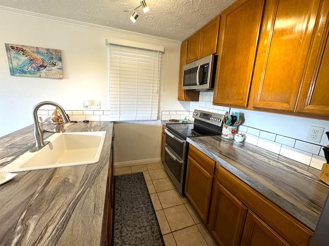 kitchen with appliances with stainless steel finishes, a textured ceiling, crown molding, sink, and light tile patterned floors