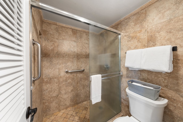 bathroom with tile walls, toilet, and a shower with shower door