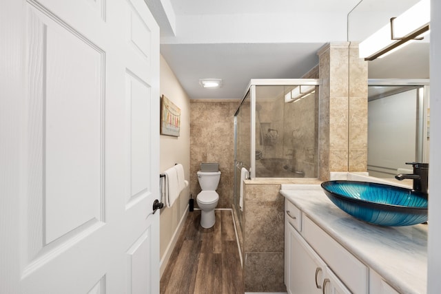 bathroom featuring vanity, wood-type flooring, a shower with door, tile walls, and toilet