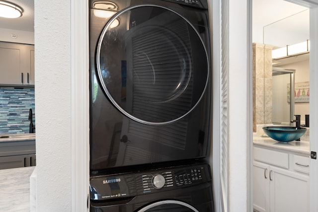 washroom with laundry area, a sink, and stacked washer / dryer