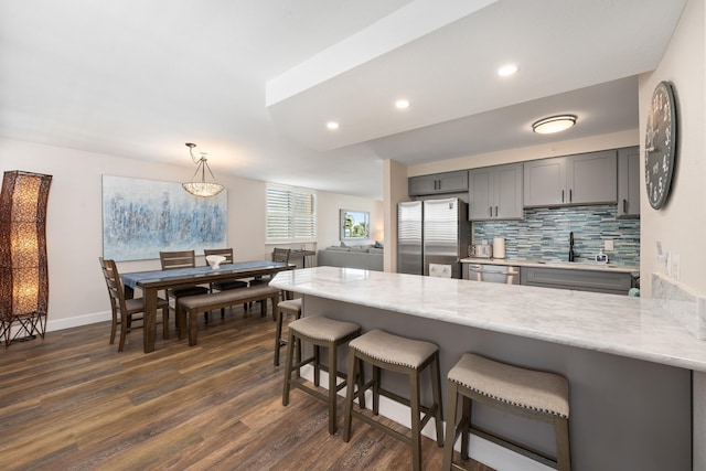 kitchen with a breakfast bar area, dark wood-style flooring, appliances with stainless steel finishes, gray cabinetry, and a peninsula