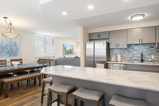 kitchen featuring decorative backsplash, gray cabinets, a kitchen bar, a sink, and stainless steel appliances