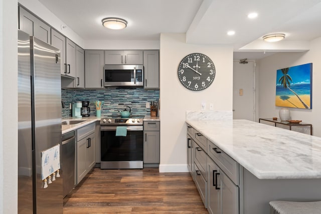 kitchen featuring gray cabinets, dark wood-style flooring, appliances with stainless steel finishes, tasteful backsplash, and a peninsula