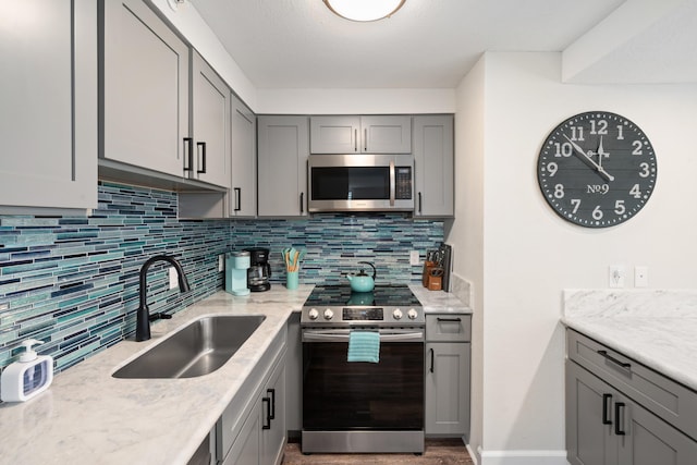 kitchen with decorative backsplash, light stone counters, a sink, gray cabinetry, and stainless steel appliances