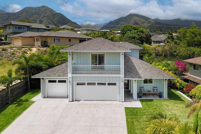 traditional home featuring a mountain view, concrete driveway, a front yard, a shingled roof, and a balcony