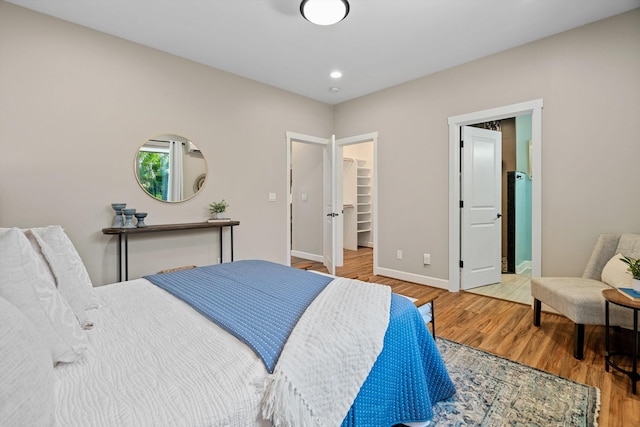 bedroom featuring a walk in closet, baseboards, recessed lighting, wood finished floors, and a closet