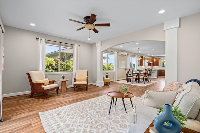 living area with a wall unit AC, recessed lighting, light wood-style flooring, arched walkways, and a ceiling fan