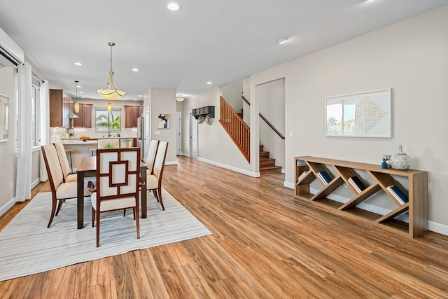 dining space with a wall unit AC, stairway, baseboards, light wood-style flooring, and recessed lighting