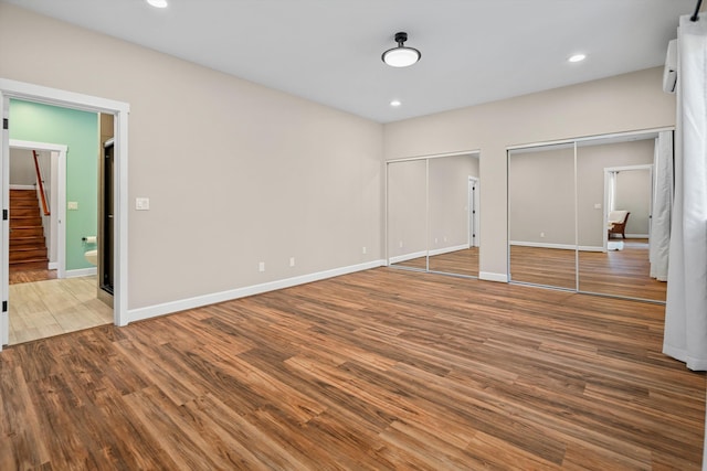 unfurnished bedroom with recessed lighting, two closets, baseboards, and wood finished floors