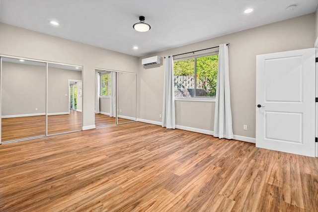 unfurnished bedroom with light wood finished floors, multiple closets, recessed lighting, and a wall unit AC