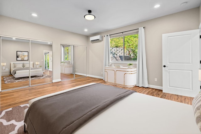 bedroom with multiple windows, wood finished floors, multiple closets, and a wall mounted AC